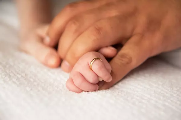 Gold ring on infant finger held by adult hands.